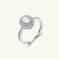 Sterling silver ring with oval moissanite center stone surrounded by double halo of sparkling stones on neutral background.