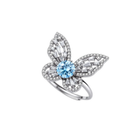 Sterling silver ring with blue moissanite center stone surrounded by clear stones in butterfly wing pattern on white background