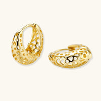 Close-up of small gold-plated hoop earrings with intricate honeycomb cutout pattern on cream background.