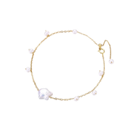 Delicate gold chain bracelet with baroque pearl centerpiece and small freshwater pearls on cream background.