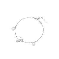 Delicate rhodium-plated silver chain bracelet with butterfly charm and two freshwater pearls on cream background