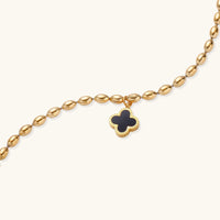 18K gold-plated oval bead bracelet with a four-leaf clover charm in mother-of-pearl or black enamel, adjustable lobster clasp, on white background.
