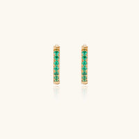 Pair of small gold huggie hoop earrings with bright green cubic zirconia stones on cream background