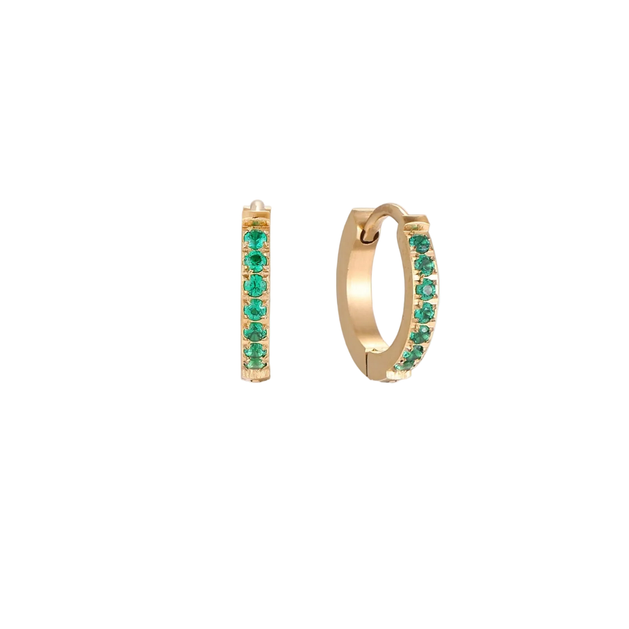 Pair of small gold huggie hoop earrings with bright green cubic zirconia stones on cream background