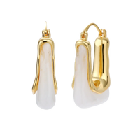 Sculptural gold-plated hoop earrings with flowing curved design and lever-back closure on cream background.