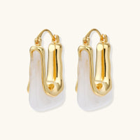 Sculptural gold-plated hoop earrings with flowing curved design and lever-back closure on cream background.