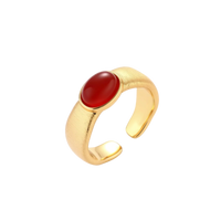 Close-up of brushed gold-plated ring with deep red oval stone, featuring adjustable band design on neutral background.