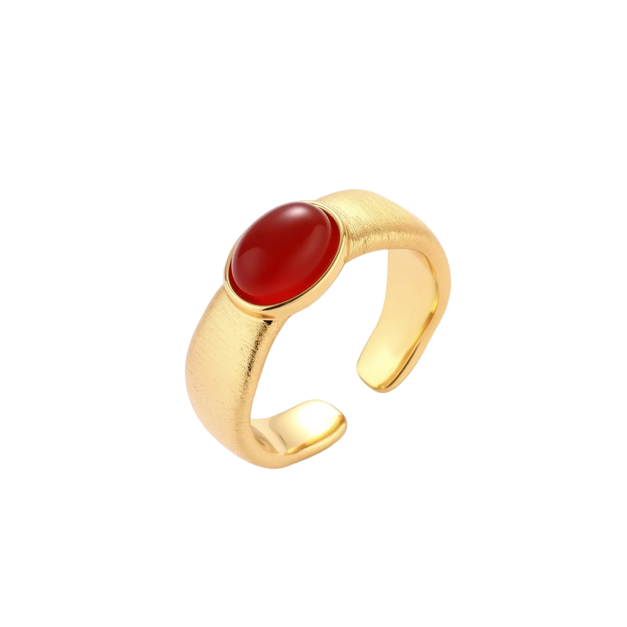 Close-up of brushed gold-plated ring with deep red oval stone, featuring adjustable band design on neutral background.