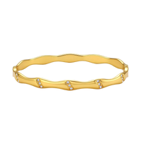 Gold-toned wavy bangle with bamboo-style segments and CZ crystal clusters on cream background. 18K plated stainless steel.