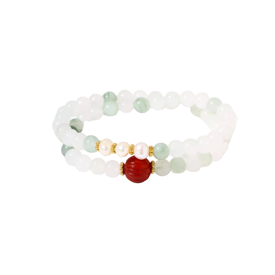 Three layered white beaded bracelets with carved orange agate lotus centerpiece and freshwater pearls on cream background.